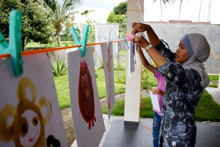 Drawings pegged on a line, a girl hanging one up, Indonesia