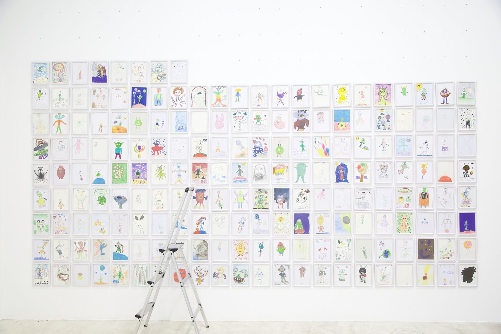 The whole wall of framed alien drawings, a stepladder in front of it, Thaillywood